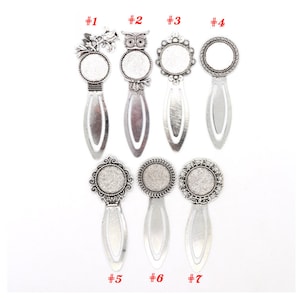 Puede incluir: Siete diseños de marcapáginas de metal plateado con un cabujón redondo de vidrio en el centro. Los diseños incluyen un búho, un diseño floral, un círculo y tres diseños ornamentados diferentes. Los marcapáginas están numerados del 1 al 7.