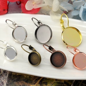 May include: Six pairs of silver, gold, bronze, and rose gold earring blanks with round glass cabochons. The earring blanks are all the same size and shape, but have different finishes.