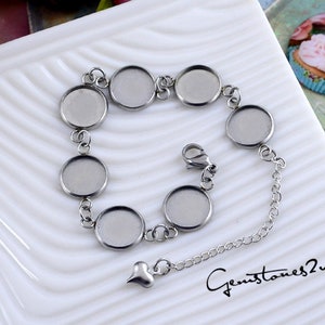 Könnte beinhalten: Ein silbernes Armband mit sieben runden, bezelbesetzten, leeren Metallanhängern. Das Armband hat einen herzförmigen Anhänger und einen Karabinerverschluss.
