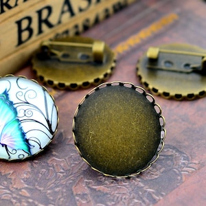 May include: Two antique gold-toned metal settings for making a cameo brooch. One setting has a clear glass dome with a butterfly design, the other setting is empty.