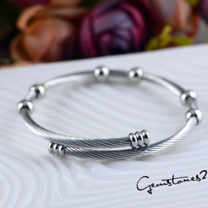 Könnte beinhalten: Ein silbernes Armreif-Armband mit einem gedrehten Kabeldesign und kleinen runden Perlen. Das Armband ist aus Edelstahl.