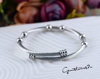 May include: A silver bangle bracelet with a twisted cable design and small round beads. The bracelet is made of stainless steel.