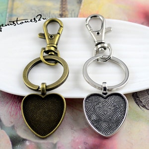 Puede incluir: Dos llaveros con dijes en forma de corazón. El llavero de la izquierda es de bronce con un dije de corazón texturizado. El llavero de la derecha es de plata con un dije de corazón liso.