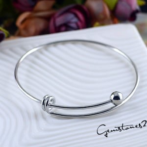 May include: A silver bangle bracelet with a small ball charm and a twisted design. The bracelet is open and ready to be worn.