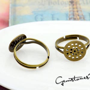 May include: Two bronze rings with a round, open, patterned bezel. The bezels are designed to hold a small cabochon or other decorative element.