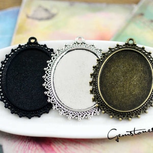 May include: Three silver-tone metal oval-shaped pendant trays with scalloped edges. The trays are black, silver, and bronze.