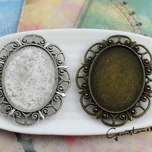 Op de afbeelding: Twee ovale metalen frames met ingewikkelde filigraanontwerpen. Het frame aan de linkerkant is zilver en het frame aan de rechterkant is brons.