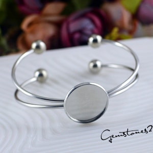 May include: A silver bangle bracelet with a round, blank, silver charm. The bracelet has a double band design and is adorned with small silver beads.