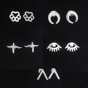 May include: Set of six silver stud earrings with different designs: paw print, crescent moon, heartbeat, eye, and triangle.