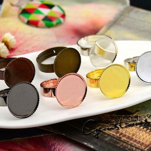 May include: Assortment of seven silver, gold, and copper ring blanks with round, clear glass cabochons. The ring blanks are adjustable and have a smooth, polished finish.