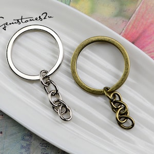 May include: Two keychains, one silver and one bronze, with a circular ring and a chain attached. The keychains are on a white surface.