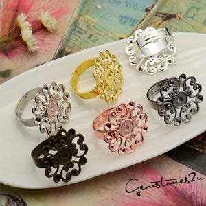 May include: Six different ring blanks with filigree designs in silver, gold, rose gold, and black. The ring blanks are on a white surface.