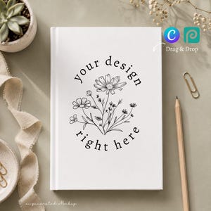 May include: A white hardcover notebook featuring a black line art illustration of a wildflower bouquet in the center, surrounded by the text "your design right here" arranged in a circular pattern. The notebook is positioned on a flat surface.