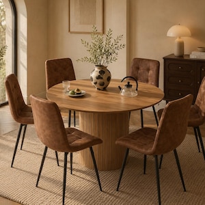 Puede incluir: Una mesa de comedor redonda de madera con base de listones verticales, rodeada de seis sillas tapizadas en color marrón con patas de metal negro. La mesa incluye un jarrón de cerámica con motivos, una tetera de cristal y un plato pequeño.