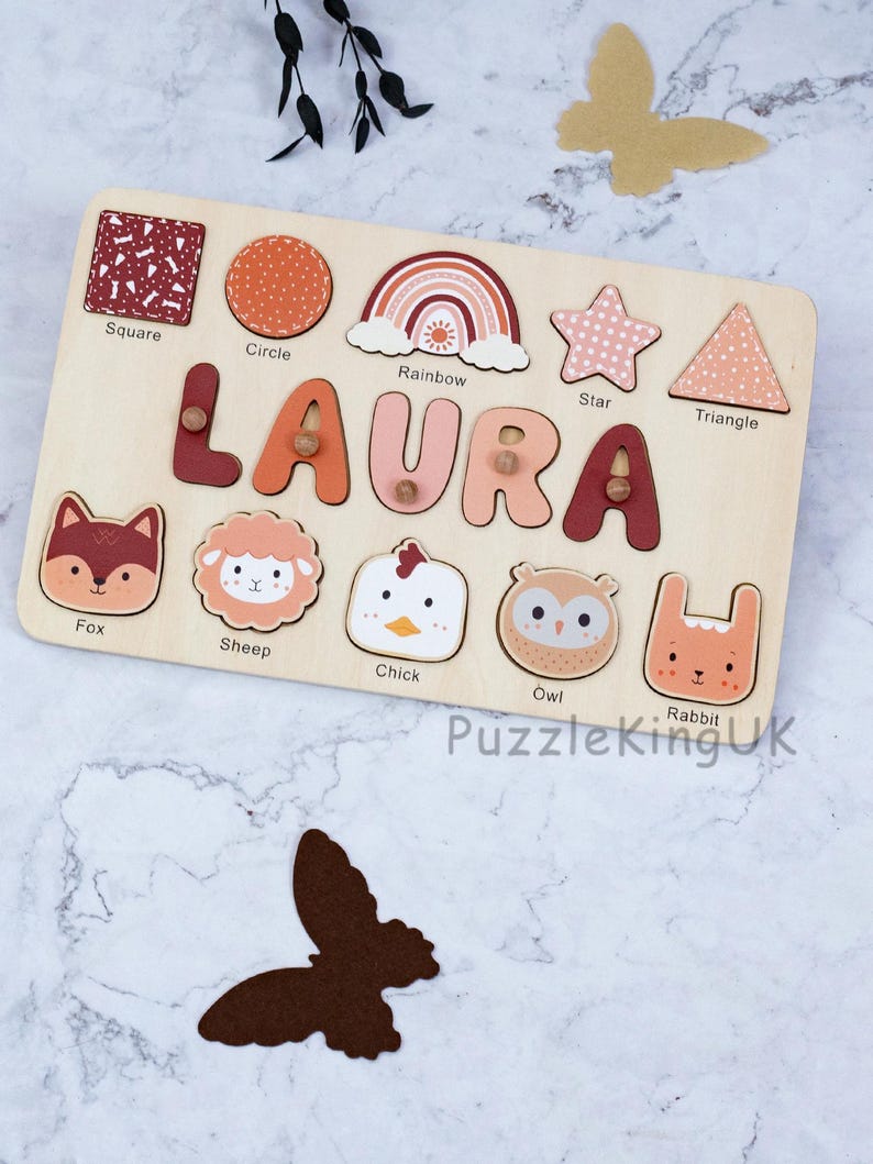 May include: A rectangular wooden name puzzle featuring the name LAURA in large, multi-colored letters with small wooden knobs. Below the name are five animal-shaped puzzle pieces: a fox, sheep, chick, owl, and rabbit, with labels underneath each.