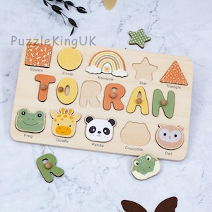 May include: A wooden name puzzle board featuring the name TORRAN in colorful letters with small wooden knobs. The board includes cutouts for shapes like a square, circle, rainbow, star, and triangle, plus animal illustrations of a frog, giraffe, panda, and owl.