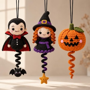 May include: Three hanging crochet ornaments featuring a vampire with a red-lined cape and a small bat, a witch with orange hair and a purple-trimmed hat, and a jack-o'-lantern pumpkin with a green stem and a dangling orange spiral tail.