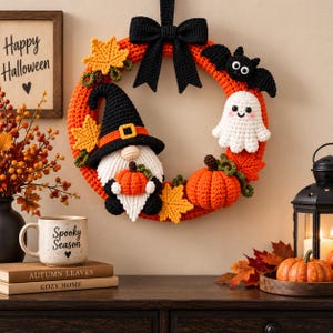 May include: A round orange crochet wreath decorated with a black bow, a gnome wearing a black hat, a white ghost, a black bat, orange pumpkins, and yellow maple leaves. The wreath is displayed alongside a sign that reads Happy Halloween.