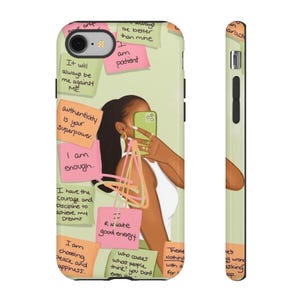 Può includere: Una cover per telefono verde chiaro con l'illustrazione di una persona che scatta un selfie allo specchio. Il design include diversi post-it colorati con affermazioni scritte a mano come Authenticity is your Superpower e I am enough.