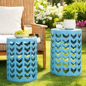 Può includere: Due tavolini cilindrici in metallo azzurro con un motivo a chevron ritagliato. I tavoli hanno un piano circolare solido e una base cava. Su un tavolo sono appoggiati una ciotola bianca con uva verde e un bicchiere di limonata.