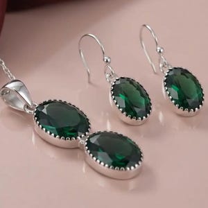Peut inclure: Un ensemble de bijoux composé d'un collier pendentif et de deux boucles d'oreilles pendantes assorties. Chaque pièce présente des pierres vert foncé à facettes de forme ovale serties dans un métal argenté avec un bord perlé.
