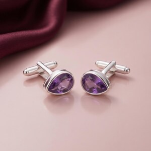 Puede incluir: Un par de gemelos de plata con piedras preciosas de amatista morada facetadas en forma de lágrima, engastadas en marcos de metal pulido. Cada gemelo incluye un mecanismo de cierre de barra en T articulado en la parte posterior.