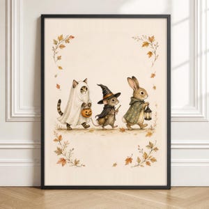 Peut inclure: Une impression d'art encadrée représentant un chat déguisé en fantôme tenant une citrouille, une souris avec un chapeau de sorcière et une cape tenant un balai, et un lapin en cape étoilée tenant une lanterne, entourés de feuilles d'automne.