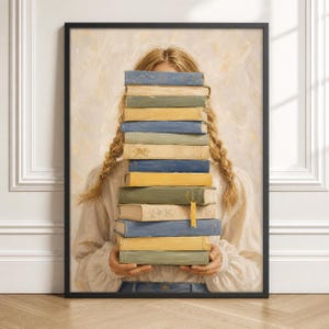 Puede incluir: Una impresión de arte mural enmarcada que representa a una persona con cabello rubio en dos trenzas sosteniendo una pila alta de libros frente a su rostro. Los libros son de varios tonos de azul, amarillo y verde, y la persona viste una camisa crema.