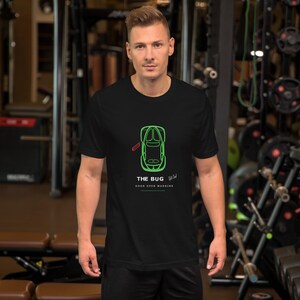 May include: A black short-sleeved t-shirt featuring a neon green top-down outline of a car with a red door indicator. Below the car, the text reads THE BUG, followed by the words DOOR OPEN WARNING in white, with a small red line graphic.