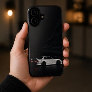 May include: A black smartphone case featuring a graphic print of a white sports car with a rear spoiler at night. The case has a dual camera cutout at the top left corner and a smooth, dark finish that covers the back of the mobile device.