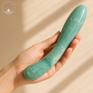 May include: A smooth, polished, light green aventurine stone wand with a curved, elongated shape and a rounded tip. The stone features natural mineral inclusions and a glossy finish. A circular logo in the top left corner reads PURE QUARTZ.