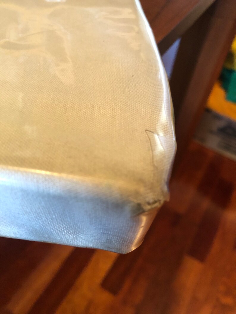 K&ouml;nnte beinhalten: Nahaufnahme einer Ecke einer hellfarbigen Tischplatte aus Metall. Die Oberfl&auml;che hat eine subtile Textur und einen leichten Glanz. Die Kante des Tisches ist leicht verbogen.