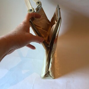 K&ouml;nnte beinhalten: Eine vintage Clutch mit floralem Muster, einem silbernen Verschluss und einem wei&szlig;en Henkel.