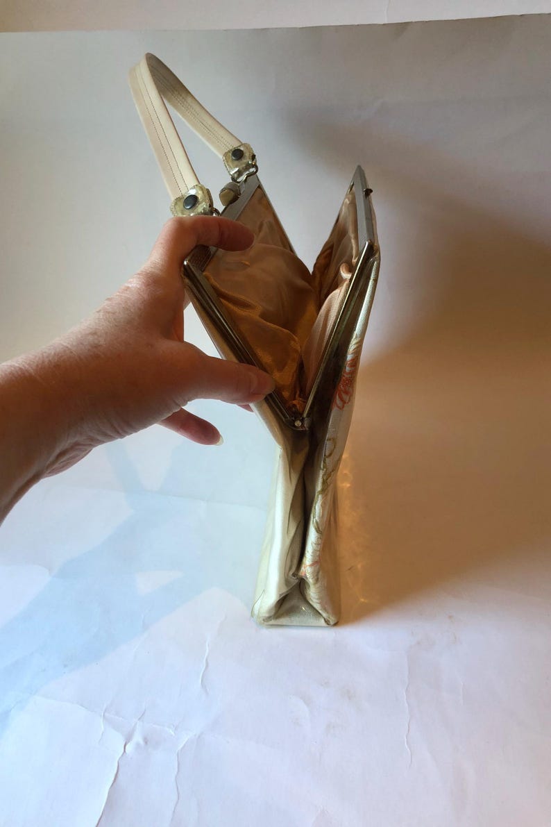 K&ouml;nnte beinhalten: Eine vintage Clutch mit floralem Muster, einem silbernen Verschluss und einem wei&szlig;en Henkel.