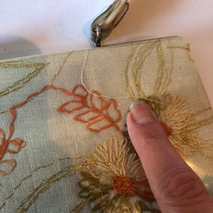 K&ouml;nnte beinhalten: Eine vintage bestickte Clutch mit einem Blumendesign in Orange-, Gr&uuml;n- und Goldt&ouml;nen. Die Tasche hat einen Metallverschluss und ein wei&szlig;es Stofffutter.
