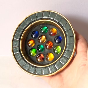 May include: A round trinket dish with a gold rim and a mosaic border. The centre is black and filled with 15 colourful glass marbles.