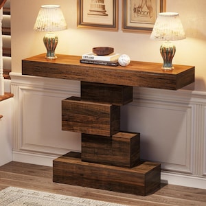 Può includere: Un tavolo console in legno marrone scuro con un piano rettangolare e una base composta da quattro blocchi rettangolari impilati e sfalsati. Due lampade da tavolo con paralumi a motivi e basi verdi poggiano sulla superficie accanto a un libro intitolato FRANK.