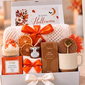 May include: A gift box containing a cream-colored knit blanket with an orange ribbon, a dessert candle, dried orange slices, a jar of honey, a box of salted caramel hot cocoa, and a ribbed mug with a gold spoon and a faux maple leaf.