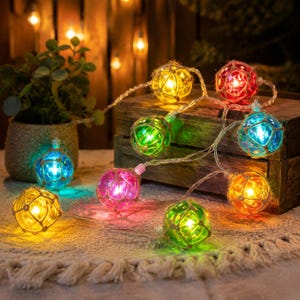 May include: A string of decorative LED lights featuring spherical glass globes wrapped in thin twine netting. The globes glow in various colors including yellow, red, green, blue, and pink, connected by a clear wire cord for indoor illumination.