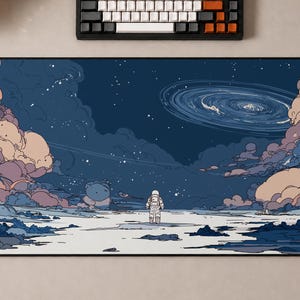 May include: A rectangular desk mat featuring a detailed illustration of an astronaut standing on a desolate, rocky surface. The scene depicts a dark blue night sky filled with swirling clouds in shades of peach and purple, with a spiral galaxy.