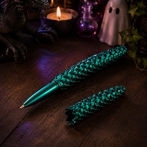 May include: A metallic emerald green ballpoint pen featuring a textured, scale-like pattern across its barrel and a matching removable cap. The pen has a smooth, tapered tip and a cylindrical body design with a distinct, repeating geometric scale motif.