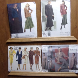 以下が含まれることがあります： 木製の棚に、4つの異なる裁縫パターン封筒が置かれています。左上の封筒は、黒と白のデザインで、「Anne Klein」と「Designer Collections」の文字が書かれています。右上の封筒は、赤と黒のデザインで、「Anne Klein」と「Designer Collections」の文字が書かれています。左下の封筒は、マルチカラーのデザインで、「Vogue's Basic Design」の文字が書かれています。右下の封筒は、マルチカラーのデザインで、「Tom and Linda Platt」と「Vogue」の文字が書かれています。