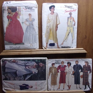 May include: Four vintage Vogue sewing pattern envelopes featuring different designs. The patterns are for a dress, pantsuit, and two dresses with different necklines and sleeves. The envelopes are in good condition with some wear and tear.