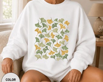 Könnte beinhalten: Ein weißes Sweatshirt mit Rundhalsausschnitt und einem sich wiederholenden Muster aus Ginkgoblättern in Salbeigrün, Olivgrün und Senfgelb. Das langärmelige Kleidungsstück hat einen gerippten Ausschnitt, Bündchen und Saum in lockerer Passform.