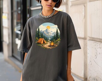 Könnte beinhalten: Ein anthrazitfarbenes Oversize-T-Shirt mit einem kreisförmigen Grafikdruck einer Berglandschaft. Das Design zeigt eine leuchtend gelbe Sonne, schneebedeckte Gipfel, einen dichten Kiefernwald, ein orangefarbenes Zelt und ein kleines Lagerfeuer.
