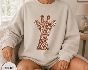 Könnte beinhalten: Ein sandfarbenes Sweatshirt mit Rundhalsausschnitt und einem braunen Grafikdruck eines Giraffenkopfes. Das Giraffenmotiv besteht aus komplizierten floralen und geometrischen Mustern, die den Hals und das Gesicht des Tieres symmetrisch bedecken.