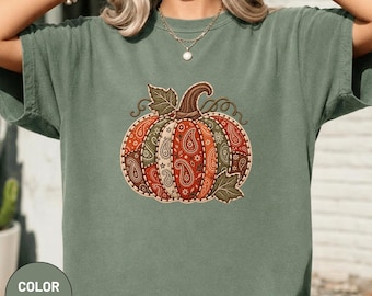 Könnte beinhalten: Ein moosgrünes T-Shirt mit kurzen Ärmeln und einem zentralen Kürbis-Motiv. Das Kürbis-Design besteht aus mehreren vertikalen Segmenten, die jeweils mit einem ausgeprägten Paisley- und Blumenmuster in Orange-, Braun- und Grüntönen verziert sind.
