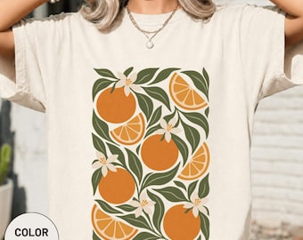 May include: An ivory t-shirt featuring a central graphic print of orange fruit, sliced orange segments, and white blossoms nestled among dark green leaves. The design is arranged in a rectangular pattern on the front of the garment.