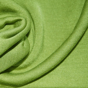 May include: A close-up of a soft, green fabric with a subtle texture. The fabric is folded and draped, creating a smooth, flowing look.