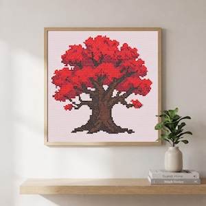 May include: A square framed cross-stitch artwork featuring a tree with a thick, dark brown trunk and vibrant red foliage. The design is set against a light pink grid background, showcasing detailed needlework stitches within a light wood frame.